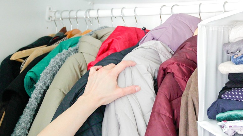 A person's arm reaching into rack of winter jackets in closet