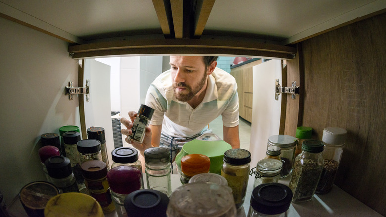 man choosing spices in cabinet