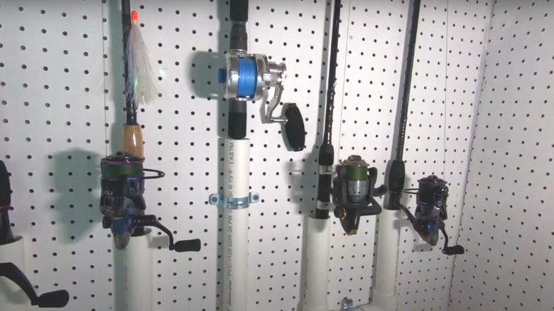 Fishing rods standing upright in PVC pipes attached to a pegboard