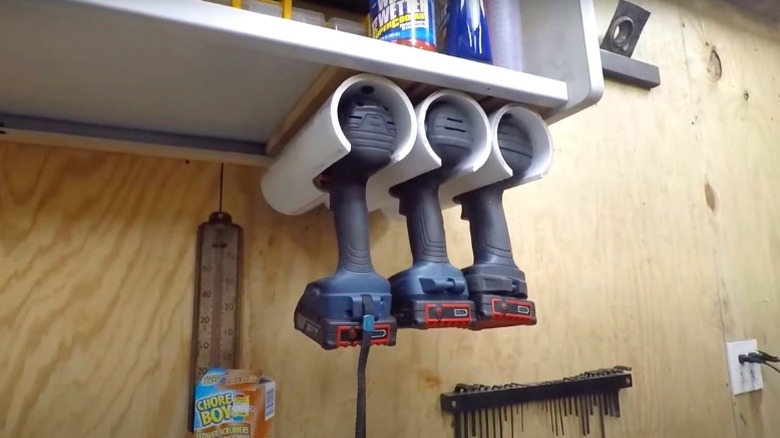 Three cordless drills hanging by their heads in PVC holders mounted under cabinet