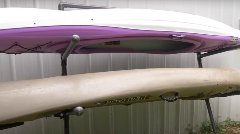 two kayaks stacked on PVC rack leaning against metal shed