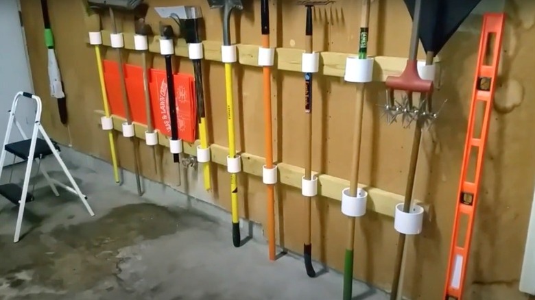 long-handled outdoor tools in PVC holders mounted on garage wall