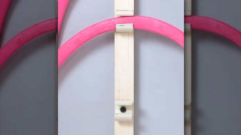 small PVC hanging hooks on narrow wood strips holding pink cord