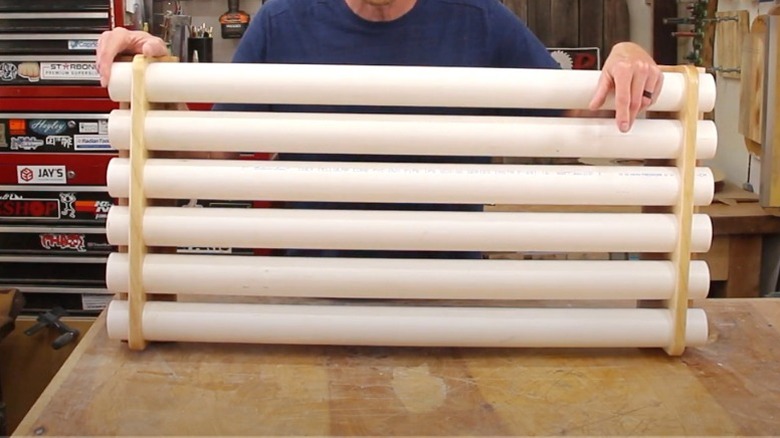 Man holding DIY PVC storage rack resting on workbench in garage