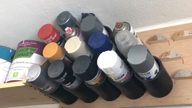 various spray paint cans in DIY PVC holder high on garage wall