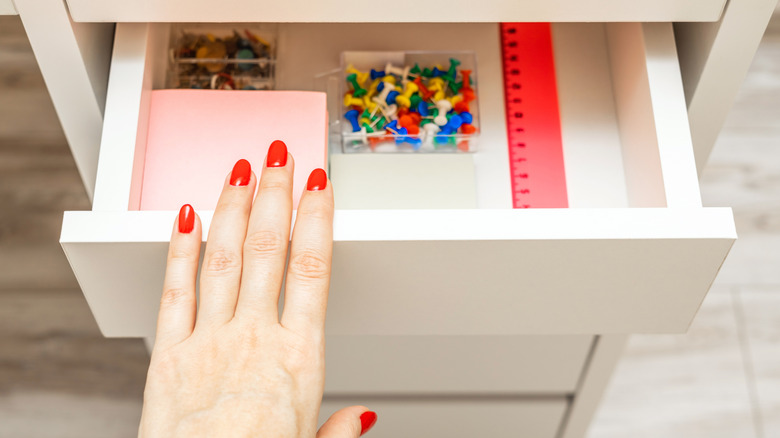 A hand with fingernails painted red opening a drawer with office supplies