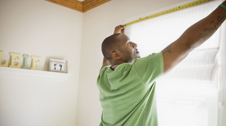 Man measuring window to hang up curtain rod