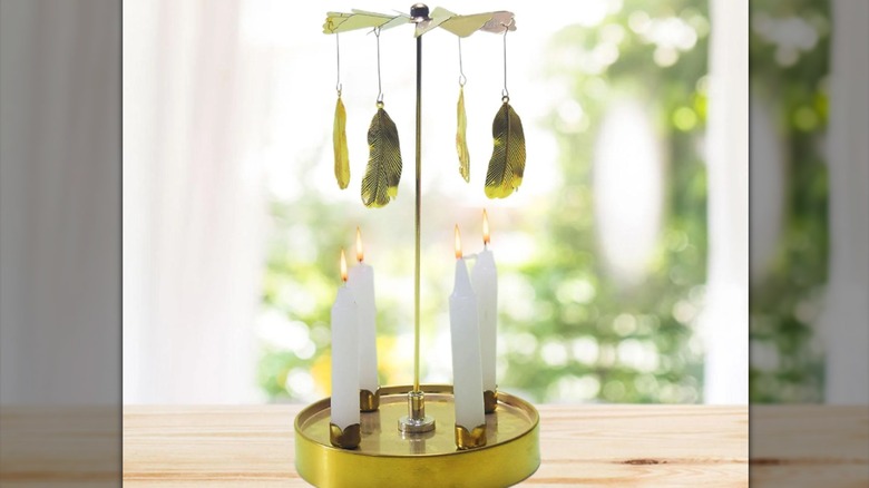 Golden rotating candle holder with feathers and lit taper candles