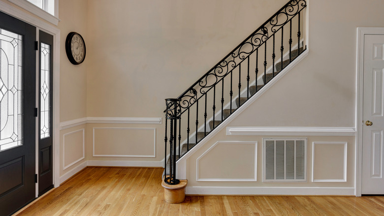 A large, empty, off white entryway with grand staircase and black door