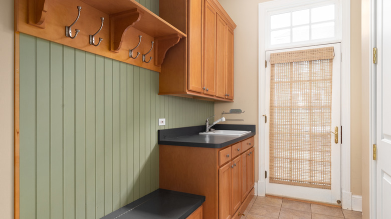 A green entryway with a bench, sink, and wood cabinets