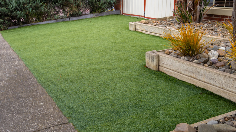 Artificial turf is in front of retained beds containing grasses and large river rocks