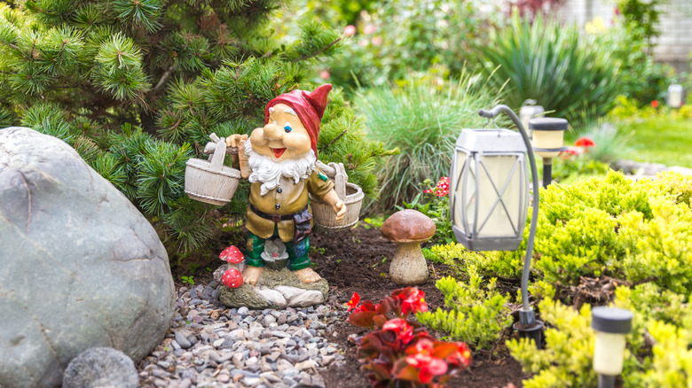 A colorful garden gnome is situated in a cluttered garden next to decorative lights