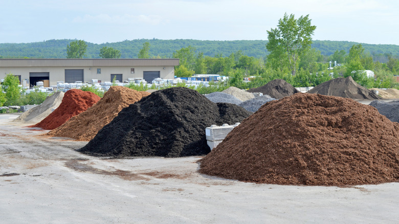 Five large piles of colored garden mulch are in front of a warehouse