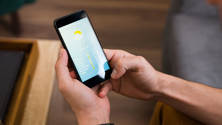 hands holding phone with weather app on screen