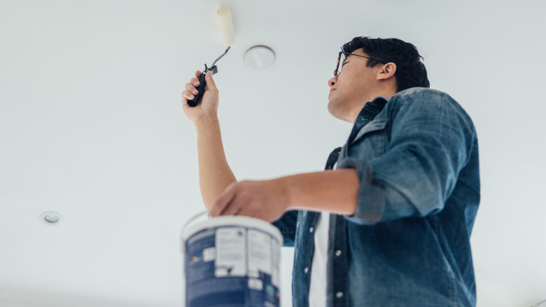 man in blue shirt painting ceiling with roller