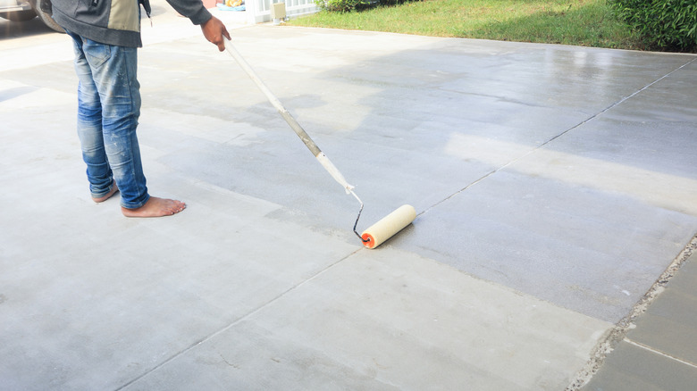 person in jeans painting driveway with a roller