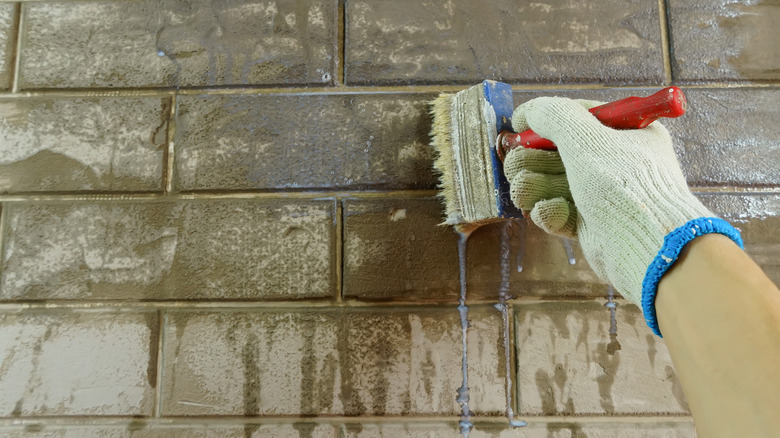 gloved hand applying stain to gray brick with red-handled brush