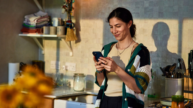 woman standing in kitchen looking at phone