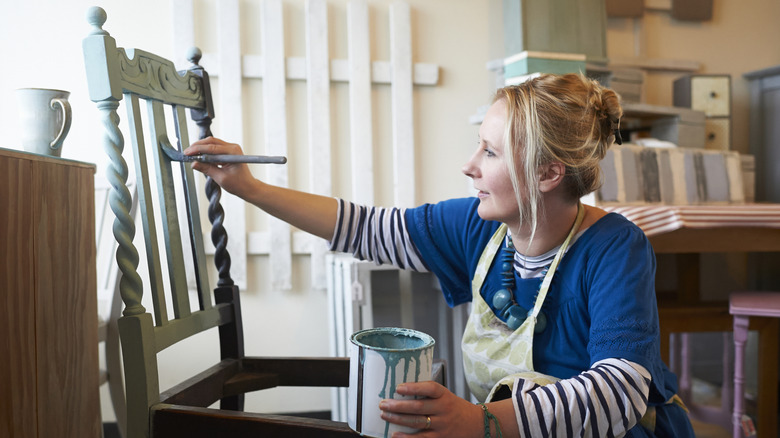 A female furniture maker paints a chair in her workshop.