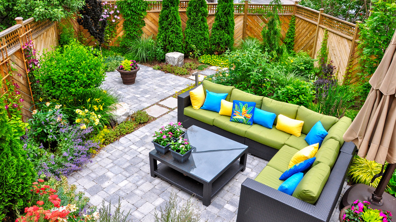 An aerial view of a colorful blossoming garden with a green patio set and bright pillows at the center.