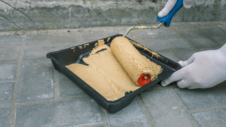 A person dips a roller into a tray of paint outside