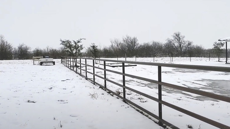 A pipe fence encloses the outdoor space and yard of a rural home.