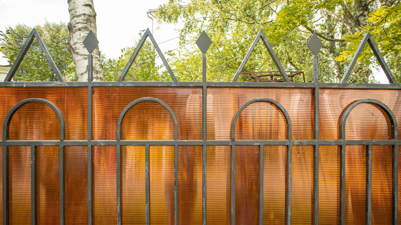 A tubular steel privacy fence with amber colored polycarbonate sheeting mounted to it.