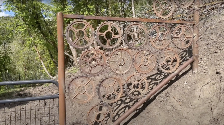 A section of a pipe fence filled with old metal cogs from a junk yard.