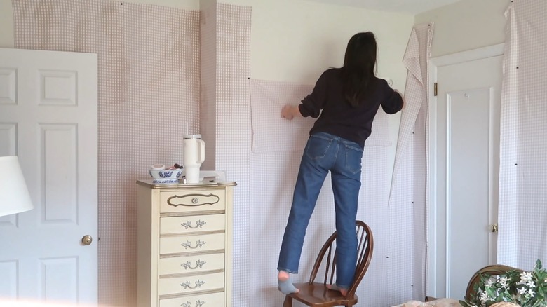 A woman putting up a plaid fabric as wallpaper in her bedroom