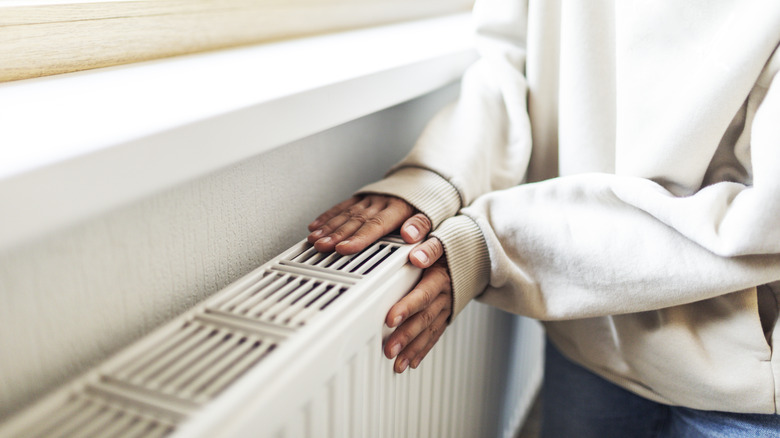 Woman heating hands on a white radiator