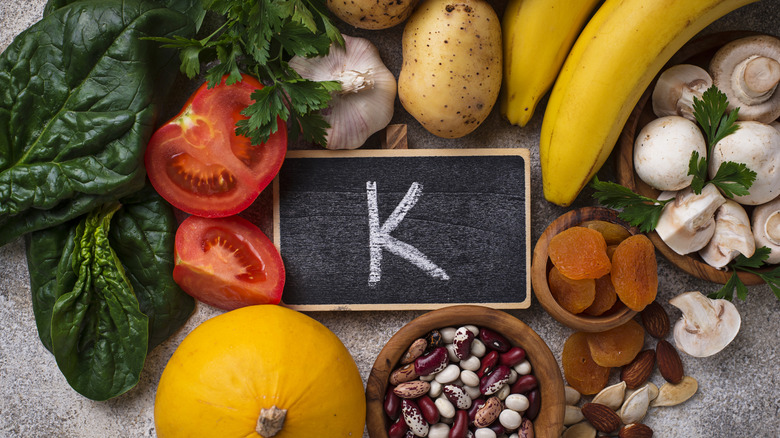 A selection of foods high in potassium including spinach, tomatoes, garlic, potatoes, bananas, mushrooms, dried fruits and nuts