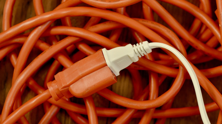 A small white electrical cord is plugged into a tangled mess of an orange extension cord