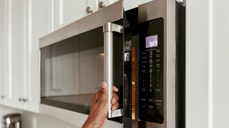 A hand closes the door of an over-the-range microwave