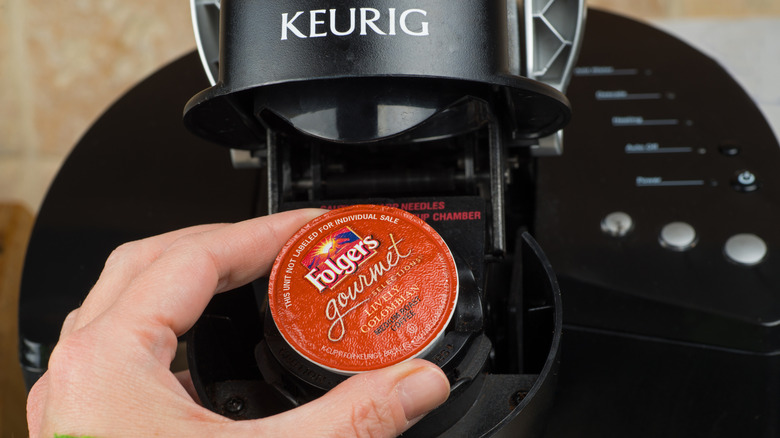 Person holding a red Folgers coffee pod that they are about to put into their Keurig coffee machine.