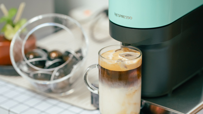 Black and teal Nespresso machine making a layered iced coffee drink.