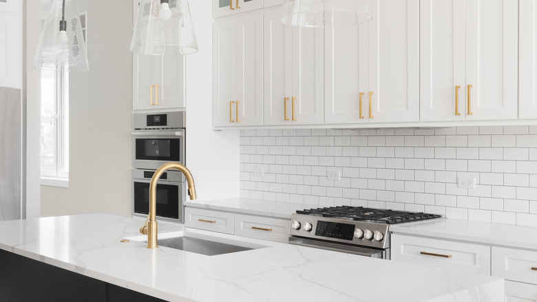 A kitchen detail with white cabinets, a large black island, gold hardware,