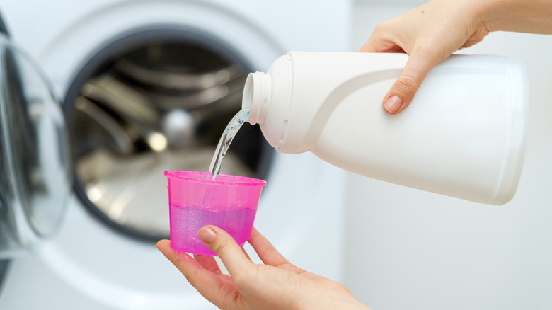 A person pouring laundry detergent in front of a washer