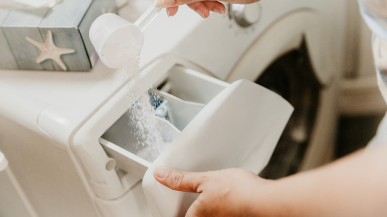 A person pouring powdered detergent into the washer