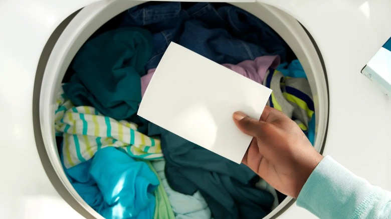 Hand holding laundry sheet in front of washing machine full of clothes