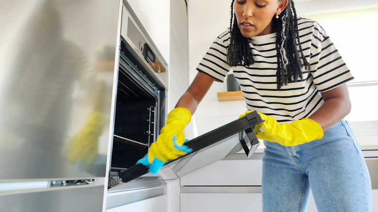 Woman cleaning oven door of her stainless steel oven