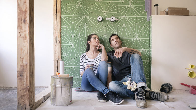 A man and woman sit in front of a tile wall admiring their work