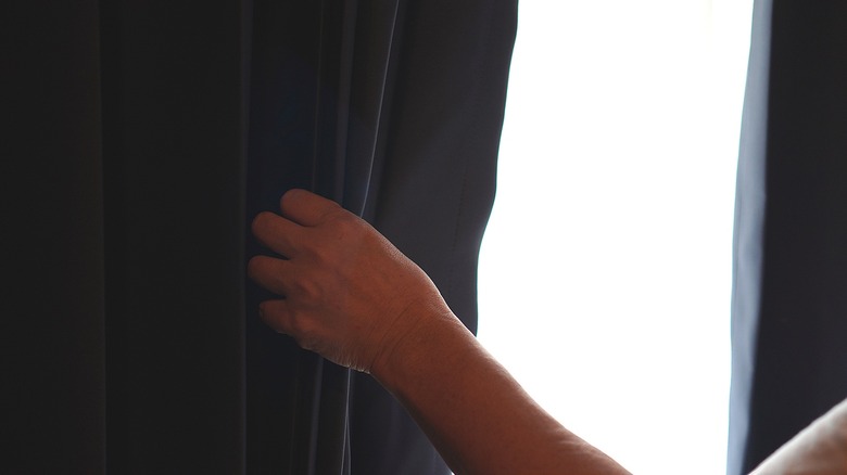 Hand pulling back a curtain over a sunny window