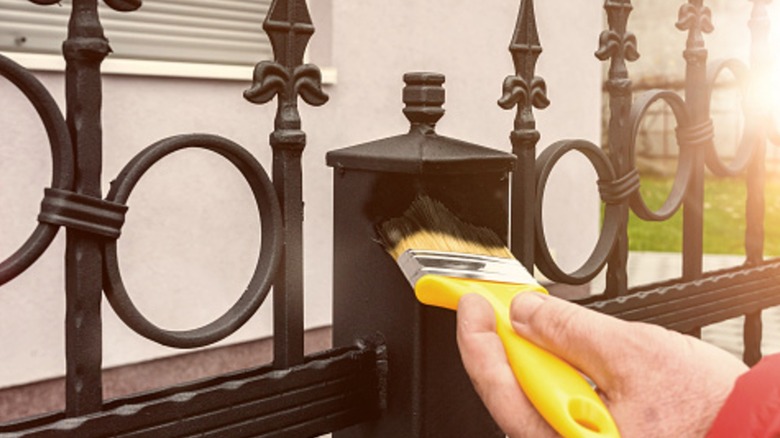 Person with a yellow paint brush sealing an iron fence