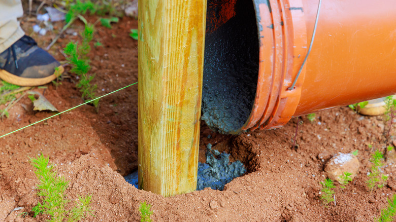 person pouring concrete around fence post from an orange bucket