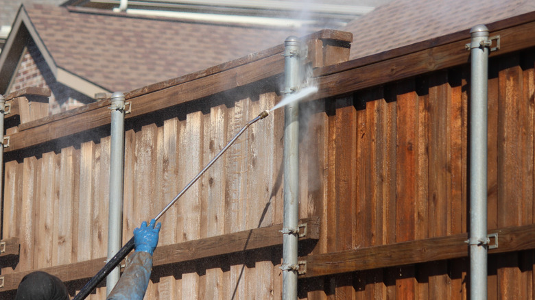 Person pressure washing a tall wooden fence