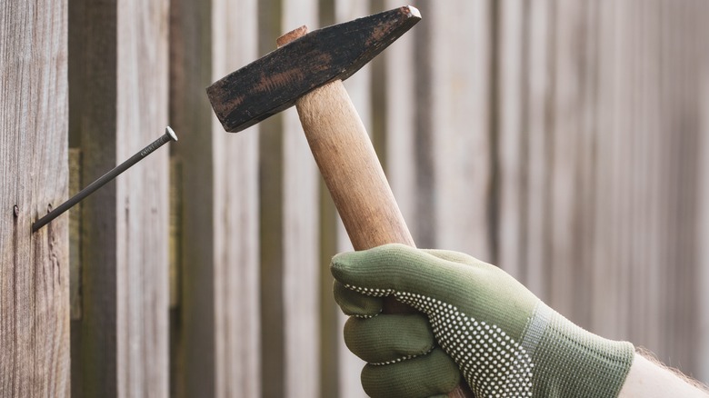 A person hammering a nail into a timber fence