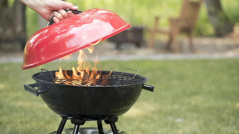 Person removing red lid from small black grill