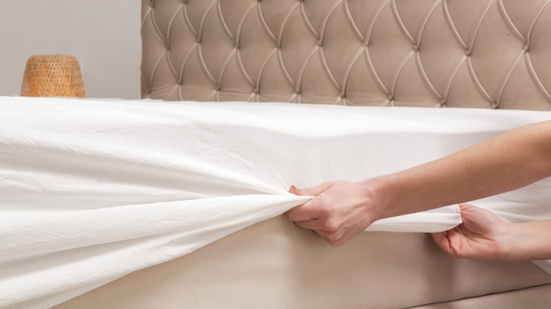 person pulling fitted sheet over mattress