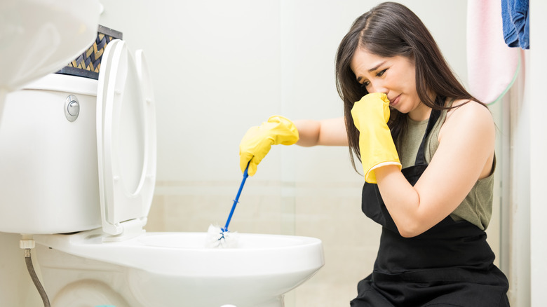 person cleaning toilet pinching nose