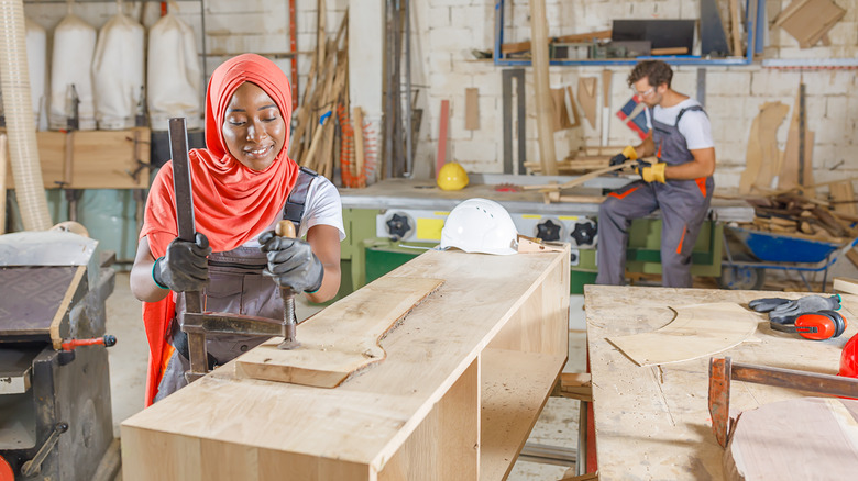 A woman using a clamp to hold a board down